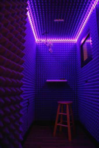Soundproof recording booth with purple acoustic foam and neon lighting. Cozy and modern design.
