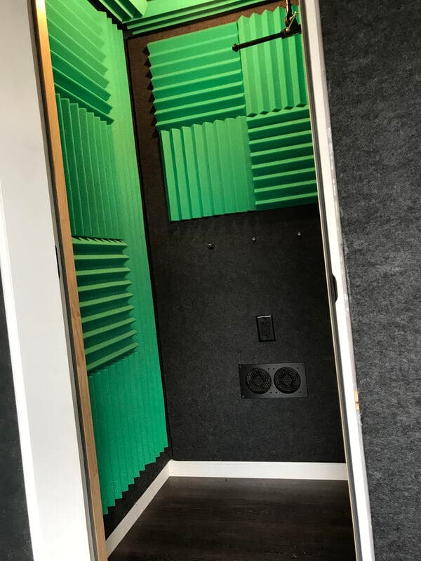 Soundproof recording booth with bright green acoustic panels and dark walls.