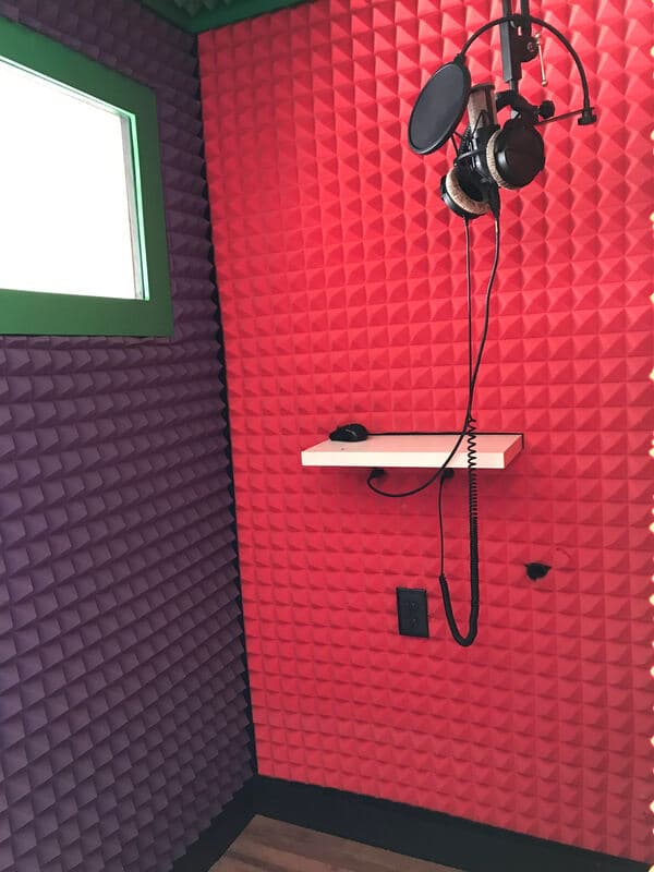 Recording studio booth with vibrant red and purple acoustic foam, microphone, and headphones.