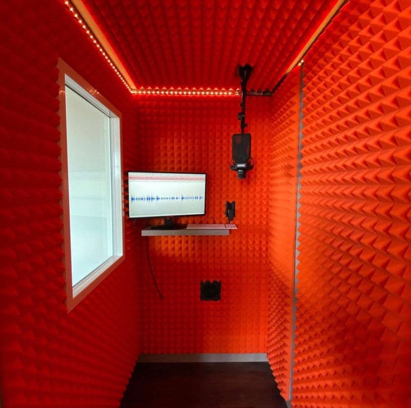 Vibrant orange soundproof recording booth with monitor and microphone setup.
